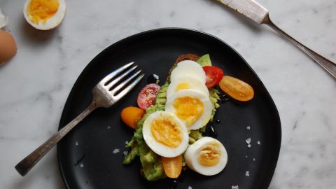 egg and avocado toast on black plate with marble counter