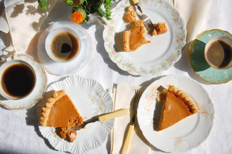 slices of pumpkin pie on table with coffee and forks