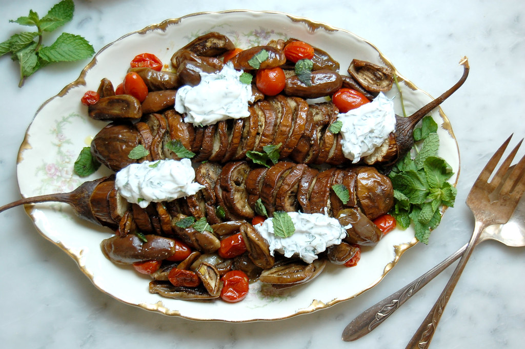 platter of hasselback eggplant parmesan with mint and tzatziki and serving utensils