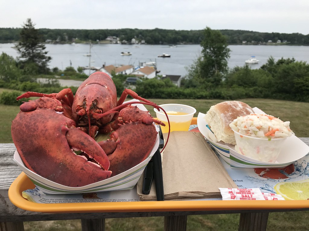 lobster and other food on tray with Maine harbor in background
