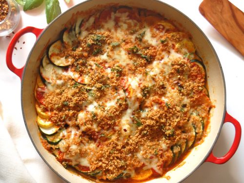 cooked zucchini and yellow squash parmesan parmigiana in red casserole with breadcrumbs and cheese