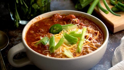 bowl of beans vegetarian chili with cheese and scallions on top