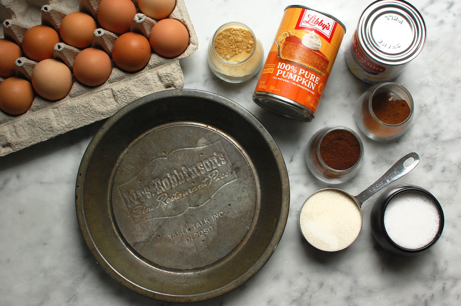 Ingredients for Libby’s pumpkin pie recipe: Libby’s 100% pumpkin, eggs, evaporated milk, sugar, cinnamon, ginger, cloves, and a pie tin on a kitchen counter.