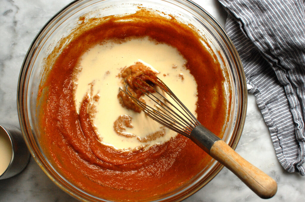 Whisking the evaporated milk into the Libby's pumpkin and spice mixture to form the custard