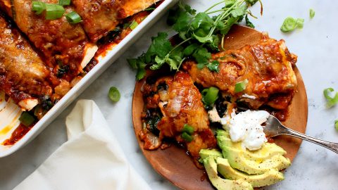 wooden plate of chicken and black bean enchiladas with avocado and cilantro
