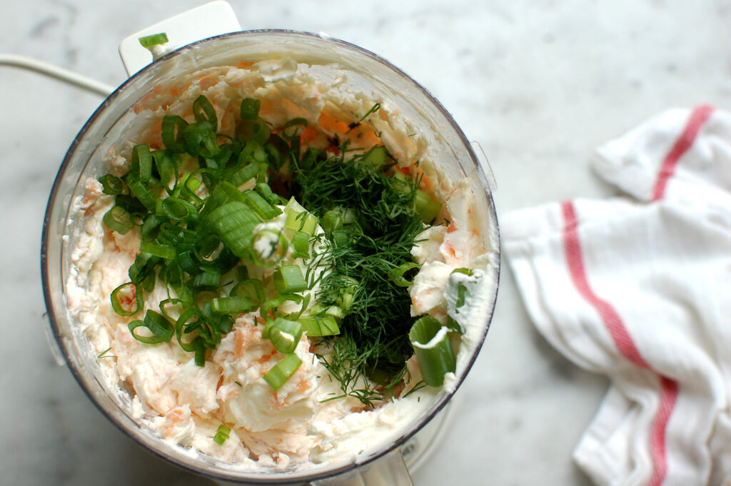 adding fresh herbs to bowl of food processor with smoked salmon cream cheese spread mixture