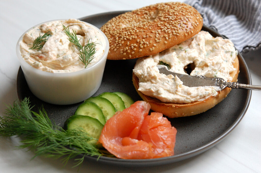 Smoked salmon cream cheese spread in a bowl with a bagel and fresh scallions and dill