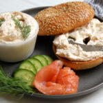 Smoked salmon cream cheese spread in a bowl with a bagel and fresh scallions and dill