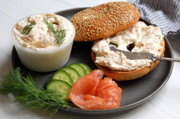 Smoked salmon cream cheese spread in a bowl with a bagel and fresh scallions and dill