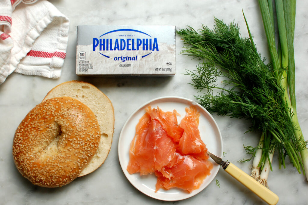 Ingredients for smoked salmon cream cheese spread: cream cheese, smoked salmon, scallions, and fresh dill with bagel on the side