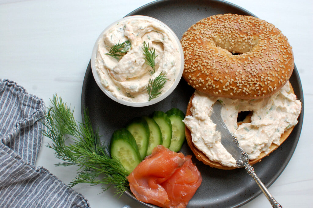 Homemade smoked salmon cream cheese spread on a toasted sesame bagel with garnish of cucumbers and dill