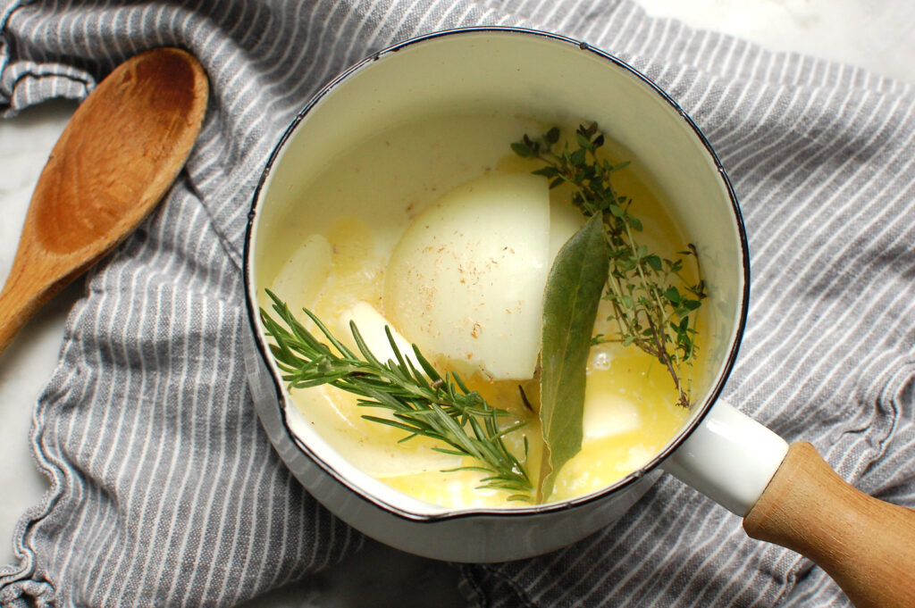small white pot of cream and milk steeping with onion, garlic, and aromatic herbs