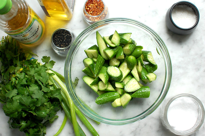 ingredients for Asian spicy cucumber salad on kitchen counter, such as cucumbers, scallions, cilantro, chili flakes, sesame oil