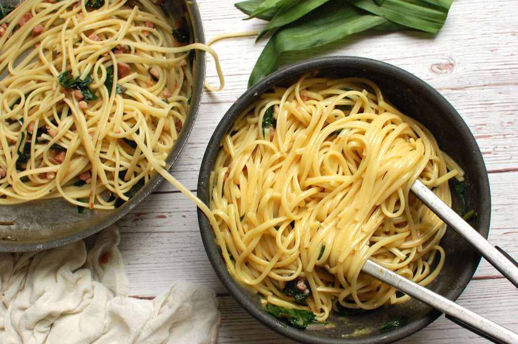 transferring the pasta cooked with pancetta and ramps into the bowl of egg and cheese carbonara sauce to finish the ramp pasta recipe