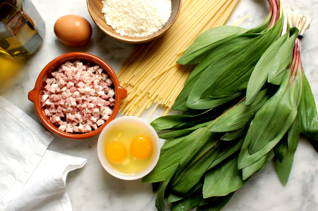 Ingredients for ramp pasta carbonara including wild ramps, pancetta, eggs, pecorino, Parmigiano, and spaghetti