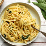 Close-up overhead of ramp pasta carbonara showing silky egg sauce and wild ramp leaves