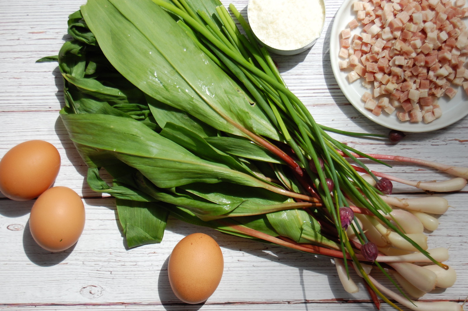 Fresh whole wild ramps with white bulbs and broad green leaves on a cutting board with other ingredients