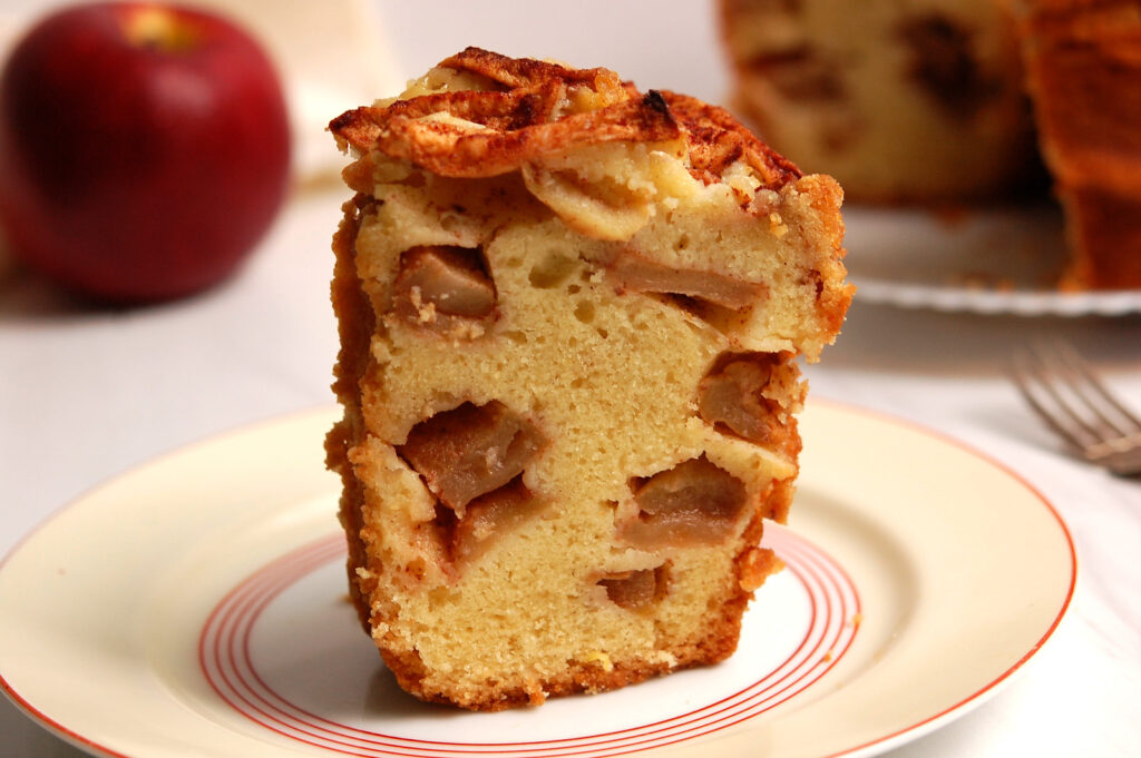 Slice of Jewish apple cake showing chunks of cinnamon apples throughout a cake with a golden, tender crumb