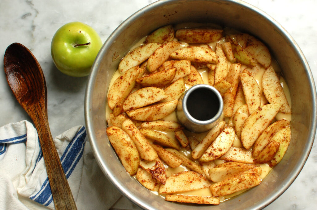 Cinnamon apple slices layered over cake batter in a tube pan before baking