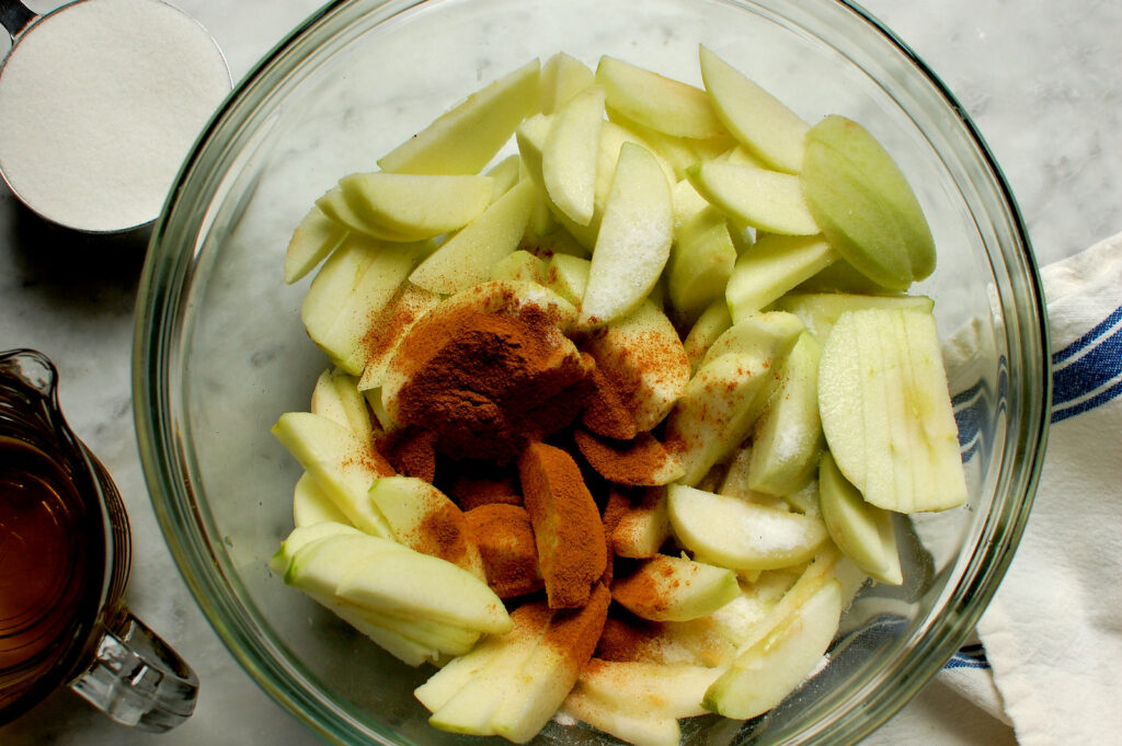 Thinly sliced apples tossed with cinnamon and sugar in a glass bowl
