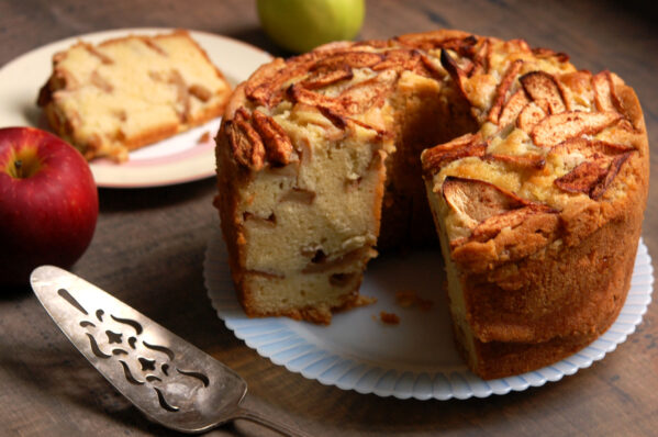 Jewish apple cake with on a cake platter, one slice cut to show layers of cinnamon apples and moist crumb