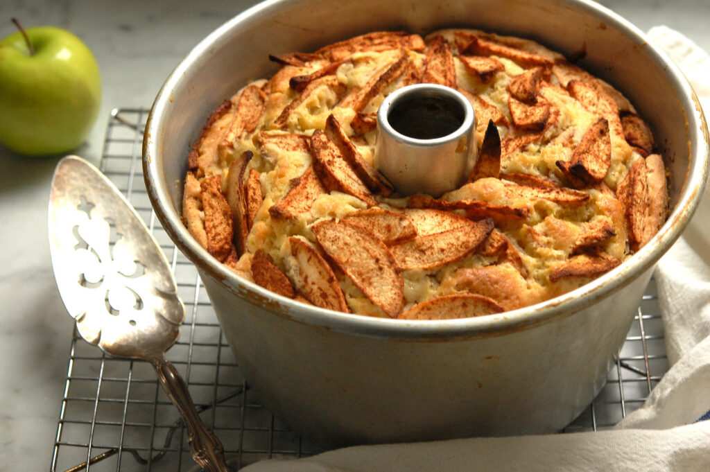 Unglazed Jewish apple cake cooling on a wire rack in tube pan with caramelized apples on top