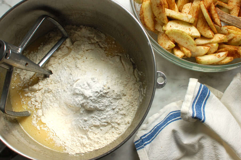 apple cake batter being mixed in bowl of electric mixer with paddle attachment