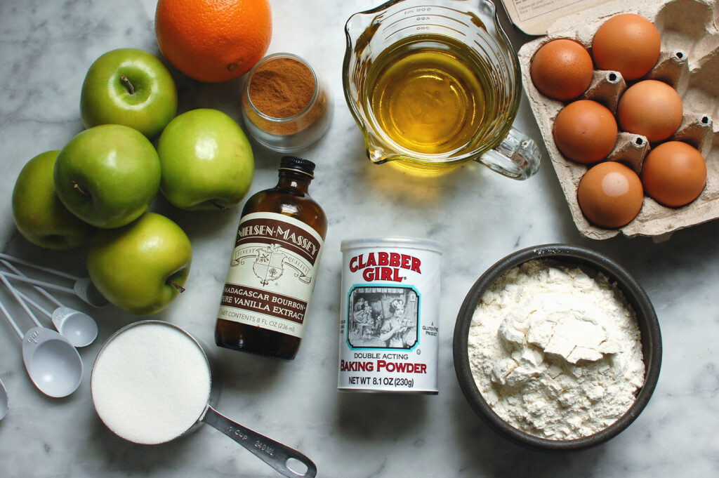 Ingredients for Jewish apple cake: Granny Smith and Honeycrisp apples, flour, sugar, eggs, oil, orange juice, cinnamon, and vanilla