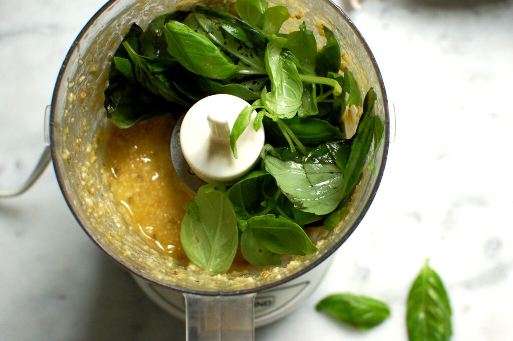 Fresh basil, pine nuts, garlic, and olive oil layered in a blender jar before being blended into pesto