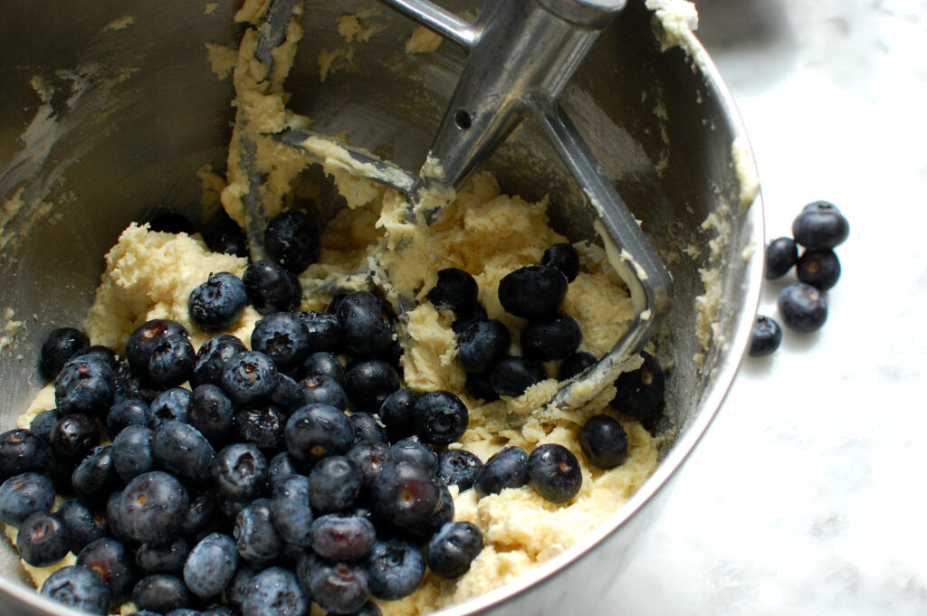 Fresh blueberries being folded into pound cake batter as one of the key steps in making the cake