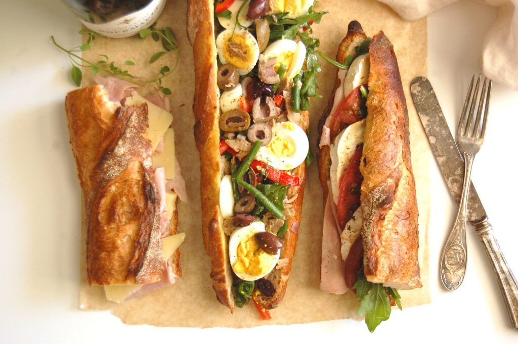 three traditional and authentic French baguette sandwiches, including jambon beurre, chevre tomate, and pain bagnat, on a kitchen countertop, ready to eat