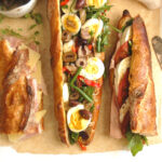three traditional and authentic French baguette sandwiches, including jambon beurre, chevre tomate, and pan bagnat, on a kitchen countertop, ready to eat