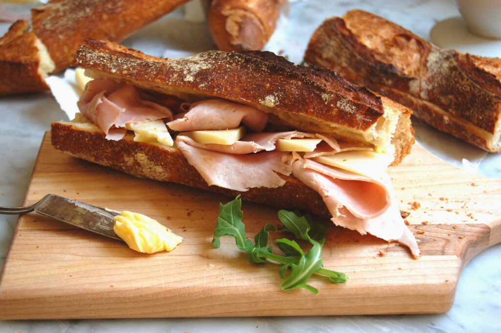 French ham and cheese jambon beurre baguette sandwich on cutting board before serving