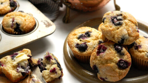 original Jordan Marsh blueberry muffins recipe, baked and served on plate with one open to show moist crumb and berries