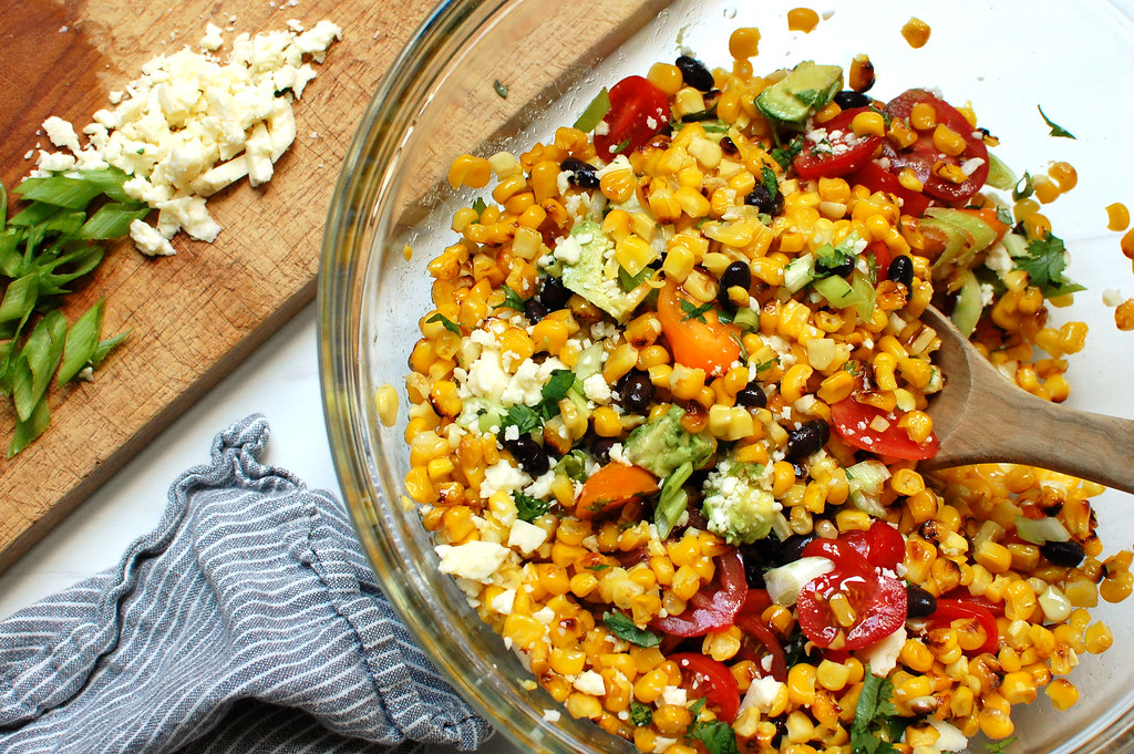 corn salad being mixed in bowl with beans and tomatoes and herbs