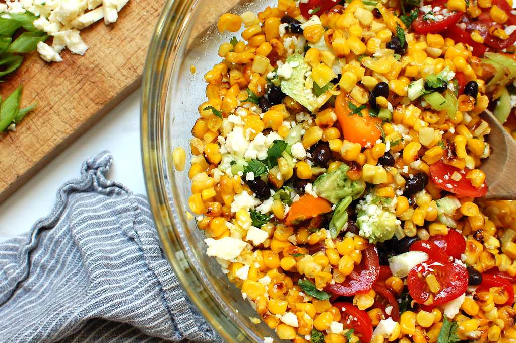 corn salad being mixed in bowl with beans and tomatoes and herbs