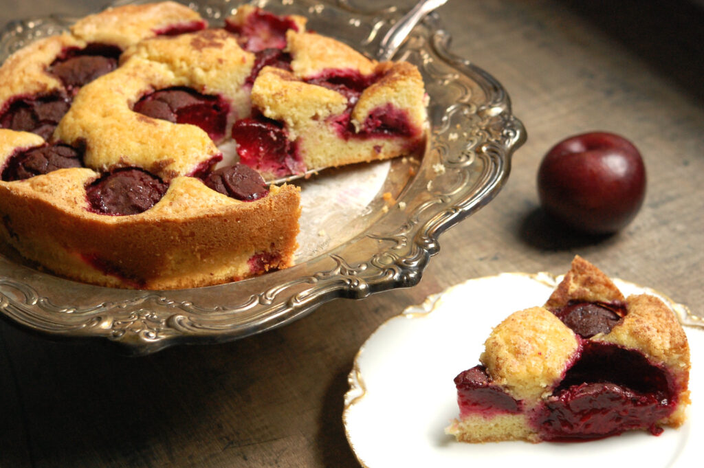 side view of baked NYT plum torte, topped with cinnamon sugar, with slice on cake plate