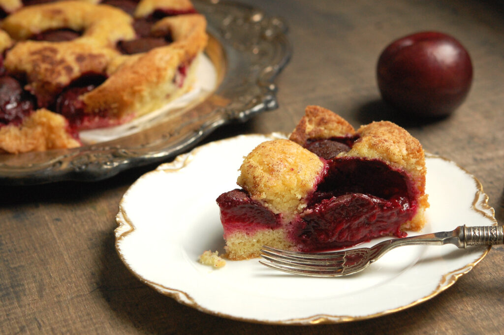 slice of baked plum cake showing cross-section of cake studded with plum chunks
