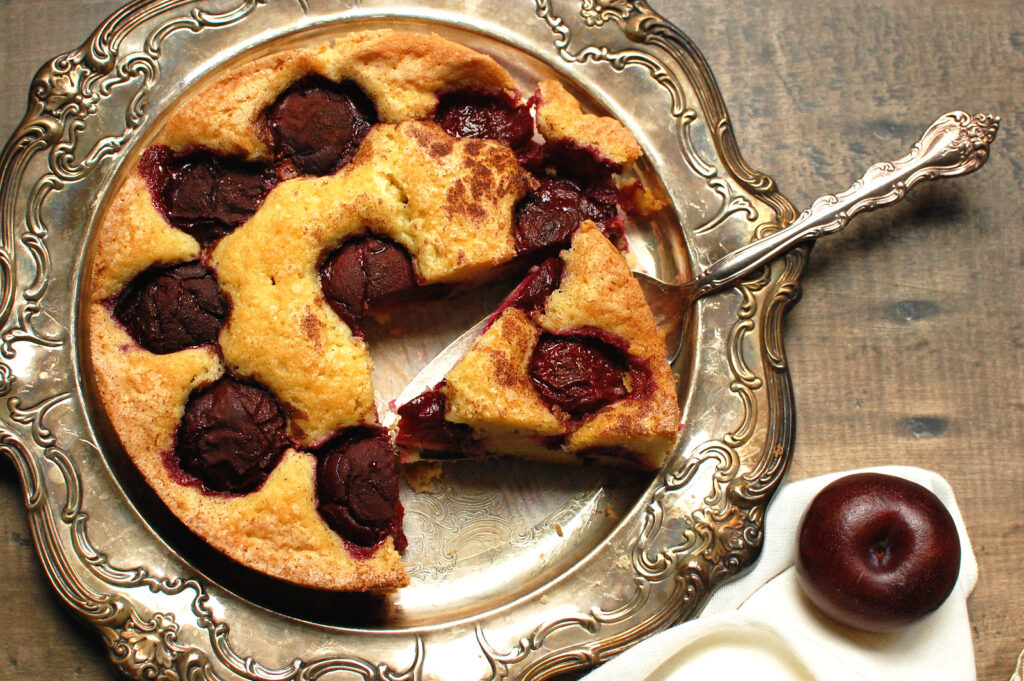 baked NYT plum torte on silver serving tray with slice cut and ready to serve, showing juicy plums