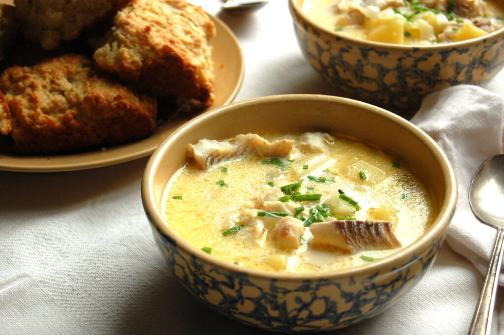 Two bowls of New England fish chowder served with buttermilk biscuits and oyster crackers