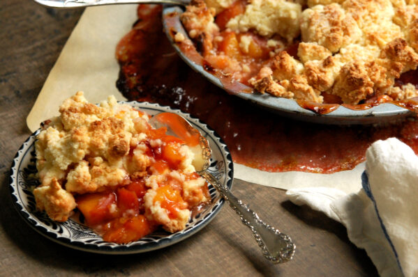 Southern peach cobbler with a golden biscuit topping and juicy peaches in a pie dish, with piece served on plate to show color and texture