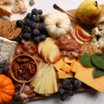 fall charcuterie board idea with cheeses, nuts, condiments, crackers, and festive seasonal garnishes on wooden board