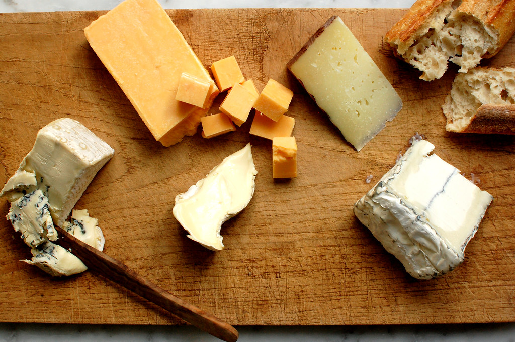 goat, cow, and sheep's milk cheeses being arranged on wooden board