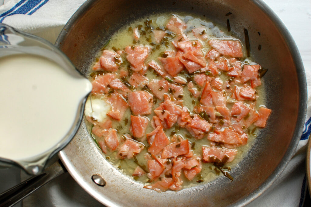 photo of the next step of making the sauce, cream being added to sautée pan and simmered with the smoked salmon