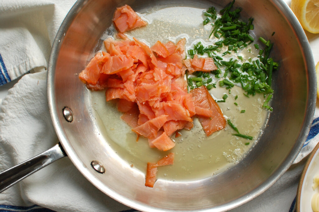 process shot of step 1 of making the sauce, sautéing chopped smoked salmon pieces and chives in butter to start the cooking process.