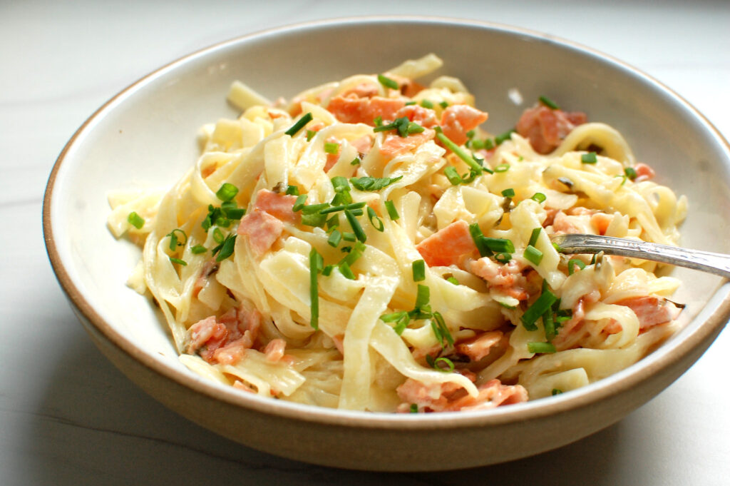 Creamy smoked salmon pasta recipe with lemon cream sauce, fresh chives, and lemon zest in a white bowl