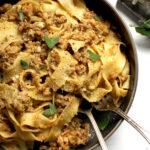 A plate of pappardelle pasta coated in glossy authentic Italian Ragù Bianco (White Bolognese) with grated cheese and sage on top.