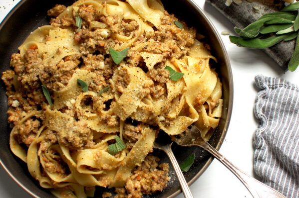 A plate of pappardelle pasta coated in glossy authentic Italian Ragù Bianco (White Bolognese) with grated cheese and sage on top.