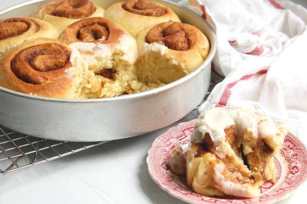homemade cinnamon roll on plate with the rest of the baked buns in casserole