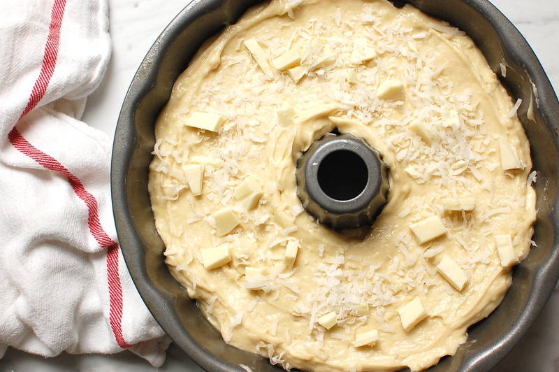 Tom Cruise Coconut Cake - Copycat Doan's Recipe white chocolate chips and coconut being scattered on top of cake batter in bundt pan before baking, like Doan's.